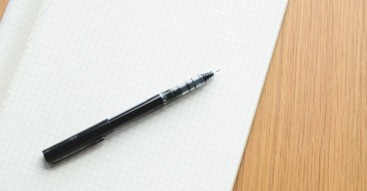 Stylo noir reposant sur un carnet à carreaux ouvert, parfait pour écrire ou concevoir.