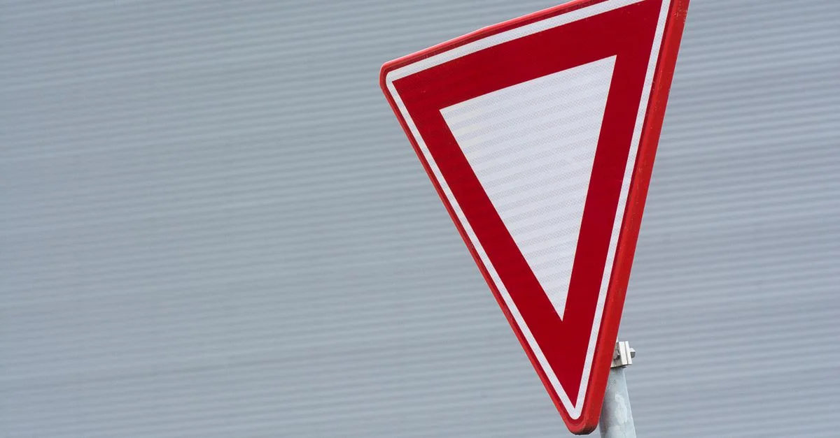 Un gros plan d'un panneau de signalisation rouge de cèdez le passage sur un fond gris texturé.